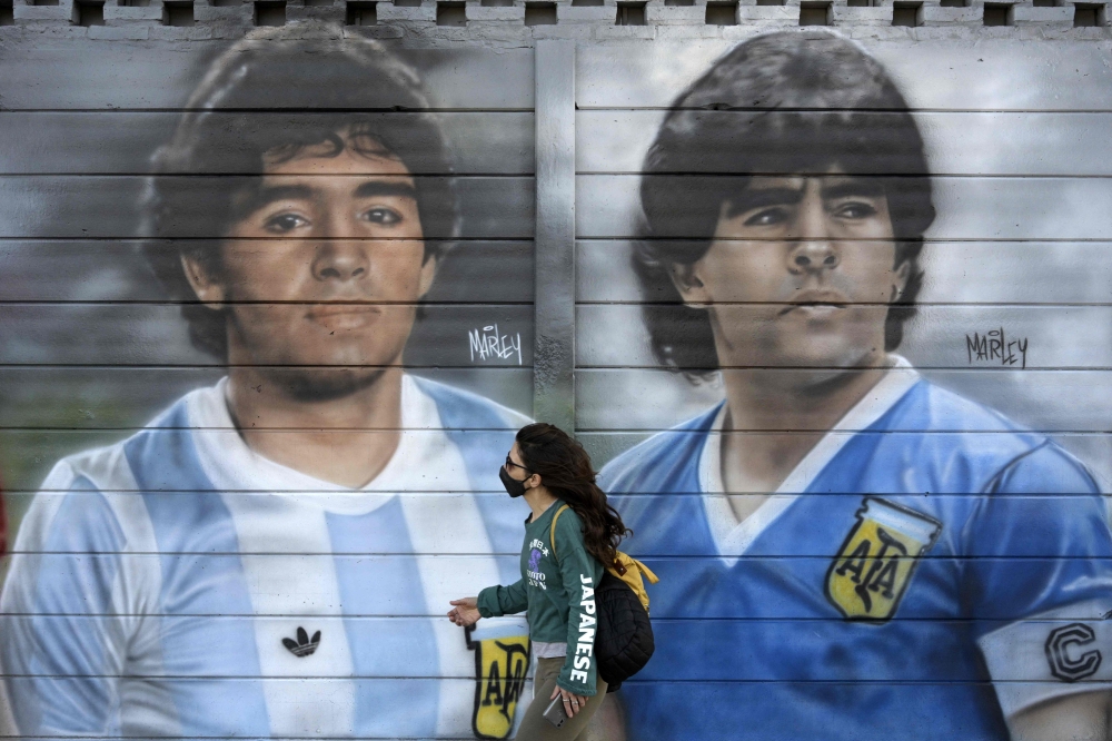 A person passes by murals painted by artist Marley outside the Diego Armando Maradona stadium as people are gathering to commemorate the Argentine legend's second goal against England during the FIFA World Cup Mexico 1986 on its 35th anniversary, in Buenos Aires on June 22, 2021. — AFP pic