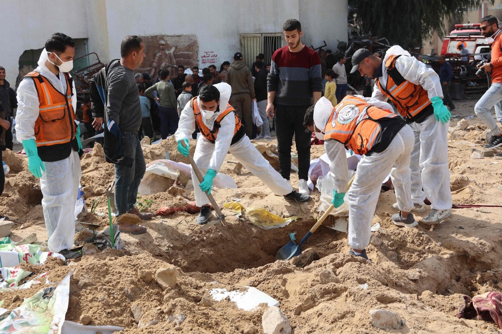 Palestinian civil defence workers uncover corpses buried in the grounds of Al-Shifa hospital in Gaza City yesterday. — AFP pic