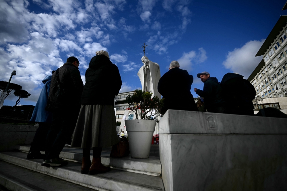 Faithfuls pray at the statue of John Paul II outside the Gemelli hospital where Pope Francis is hospitalized with pneumonia yesterday. — AFP pic