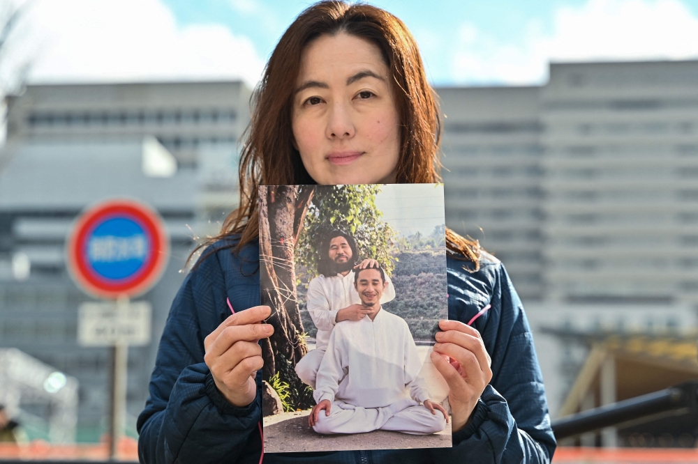 This photo taken on February 24, 2025 shows Yuki Niimi, the widow of Tomomitsu Niimi who was executed in 2018 along with other former members of the doomsday cult Aum Shinrikyo for their roles in the 1995 sarin gas attacks on the Tokyo metro system, posing with a photo of her husband (front) with cult leader Shoko Asahara, following an interview with AFP in Osaka. Only seven years into her marriage did Yuki Niimi first touch her husband — at a morgue where she collected his body after he was executed, and kissed him in a coffin. — AFP pic