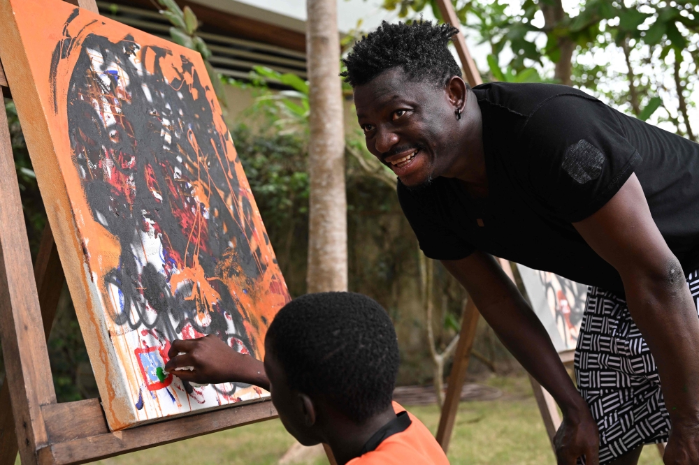 Ivorian painter Aboudia (Abdoulaye Diarrassouba) watches as a young boy paints a picture during a workshop in Assinie-Mafia on February 22, 2025. — AFP pic