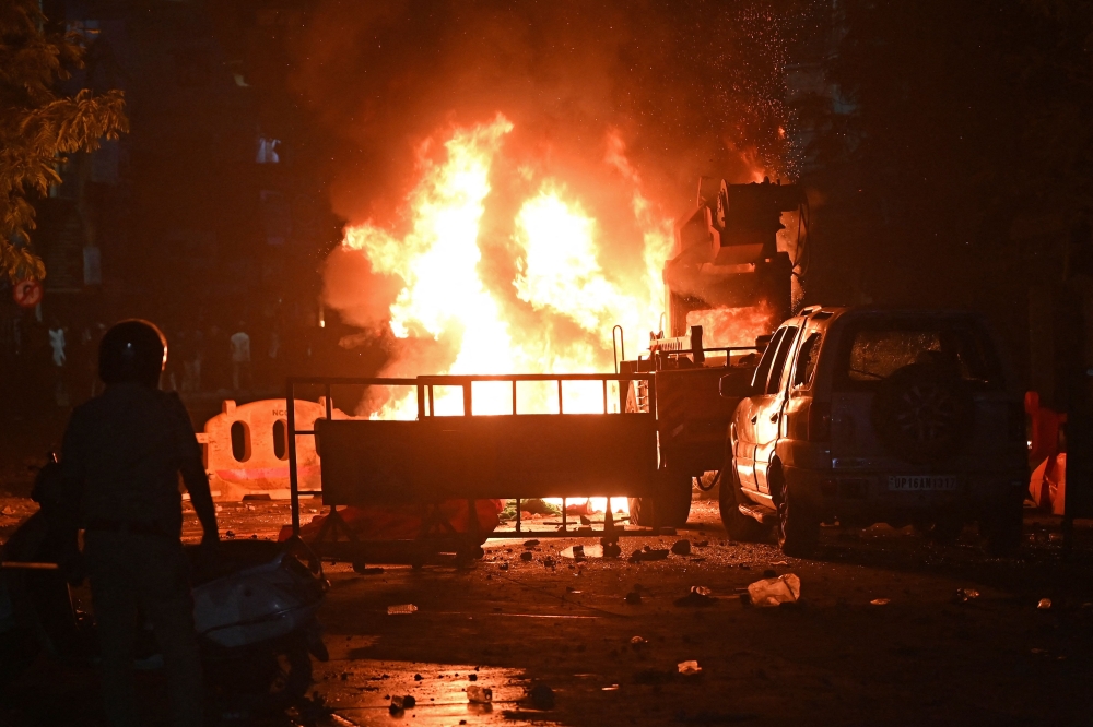 A firefighter stands near the burning vehicles set on fire following clashes at the Chitnavis Park Square area, in Nagpur on March 17, 2025. — AFP pic
