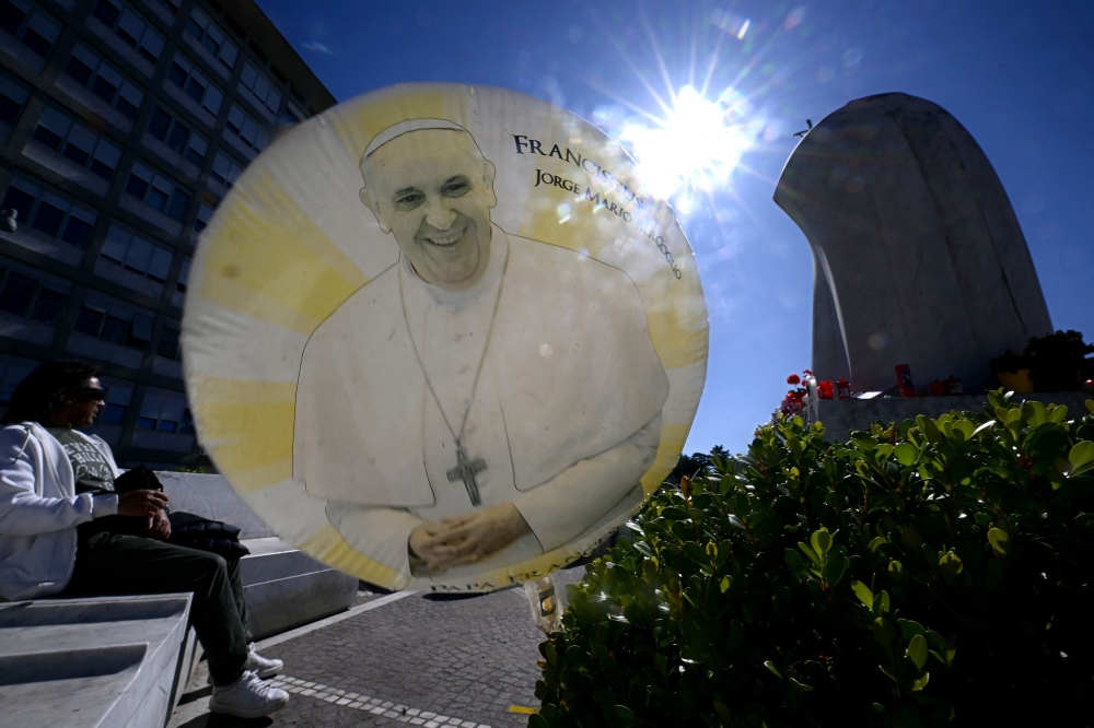 A balloon bearing an image of Pope Francis floats by the statue of the late Pope John Paul II at the main entrance of The Gemelli Hospital in Rome yesterday. — AFP pic