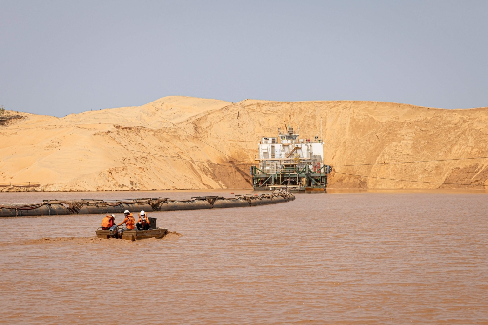 Workers approach the dredger by boat at the Eramet Grande Cote (EGC) floating Wet Concentration Plant (WCP) in the Lompoul desert in Lompoul, on February 12, 2025. The gigantic rig sucks up thousands of tonnes of mineral sands an hour, moving forward on an artificial lake created with water its pumps from deep underground. — AFP pic