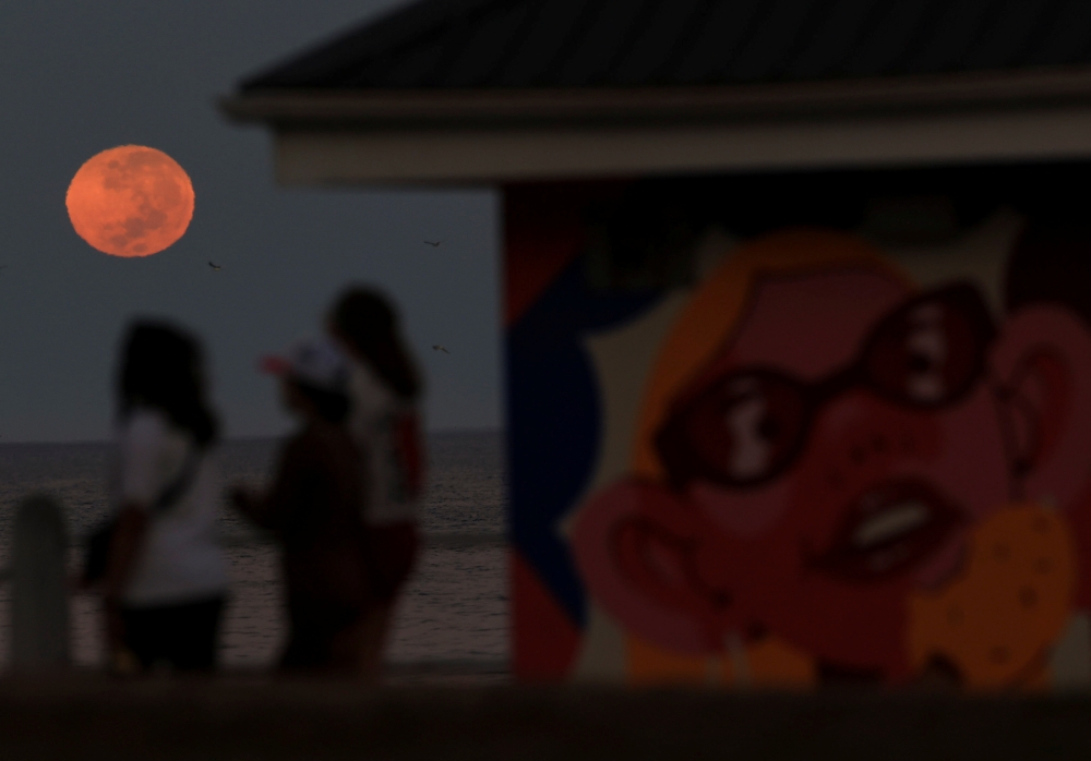 A full moon sets during a total lunar eclipse, as people walk on Sea Point promenade, in Cape Town, South Africa, March 14, 2025. — Reuters pic