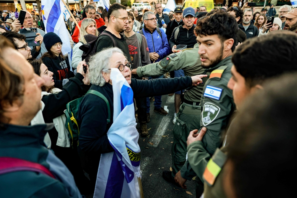 A woman carrying a flag speaks to Israeli security forces as they try to disperse a demonstration against Prime Minister Benjamin Netanyahu and calling for an end to the war in Gaza on March 19, 2025. — AFP pic
