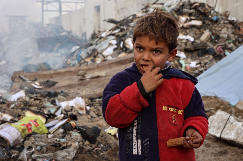 A boy looks on as he eats at a camp sheltering displaced Palestinians set up at a landfill in the Yarmuk area in Gaza City yesterday. — AFP pic