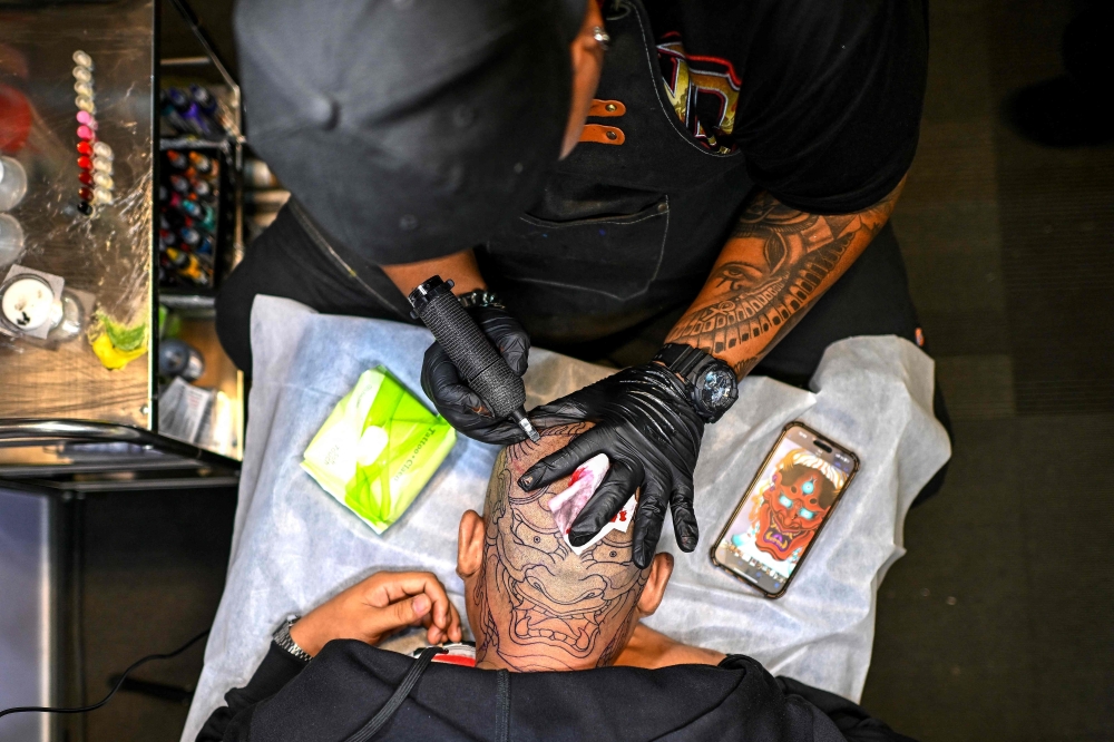 An artist works on a client’s tattoo at the Thailand Tattoo Expo 2025 in Bangkok. — AFP pic