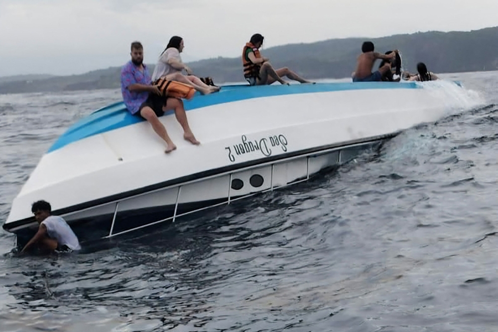 This handout from the Klungkung District Police taken on March 21, 2025 and released on March 22, 2025 shows survivors sitting on the hull of a capsized boat, as they wait to be rescued, after the snorkeling boat with tourists was hit by waves in Nusa Penida, Bali. — Klungkung District Police handout/AFP pic 