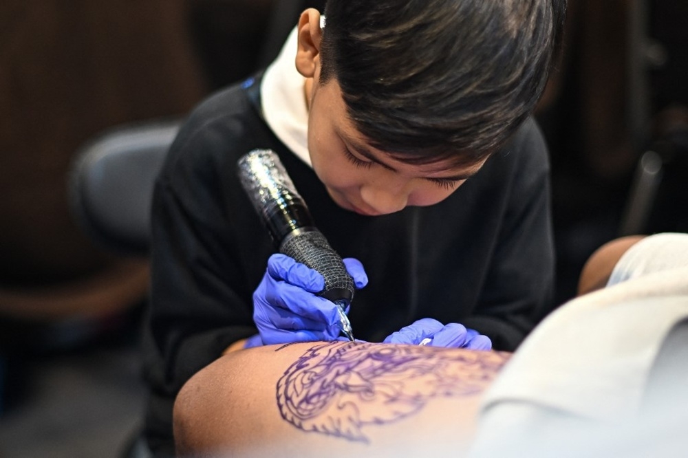 Nine-year-old Napat Mitmakorn, a Thai child tattoo artist works on his uncle’s tattoo at the 2025 Thailand Tattoo Expo in Bangkok on March 15, 2025. Wielding a cumbersome tattoo gun in child-sized hands swamped by adult-sized surgical gloves, nine-year-old Napat Mitmakorn expertly inks the pattern of a fanged serpent on a man's upper thigh. — AFP pic