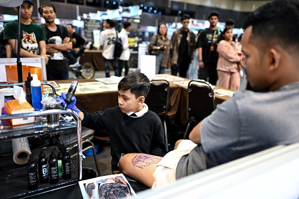 Nine-year-old Napat Mitmakorn, a Thai child tattoo artist works on his uncle’s tattoo at the 2025 Thailand Tattoo Expo in Bangkok. — AFP pic