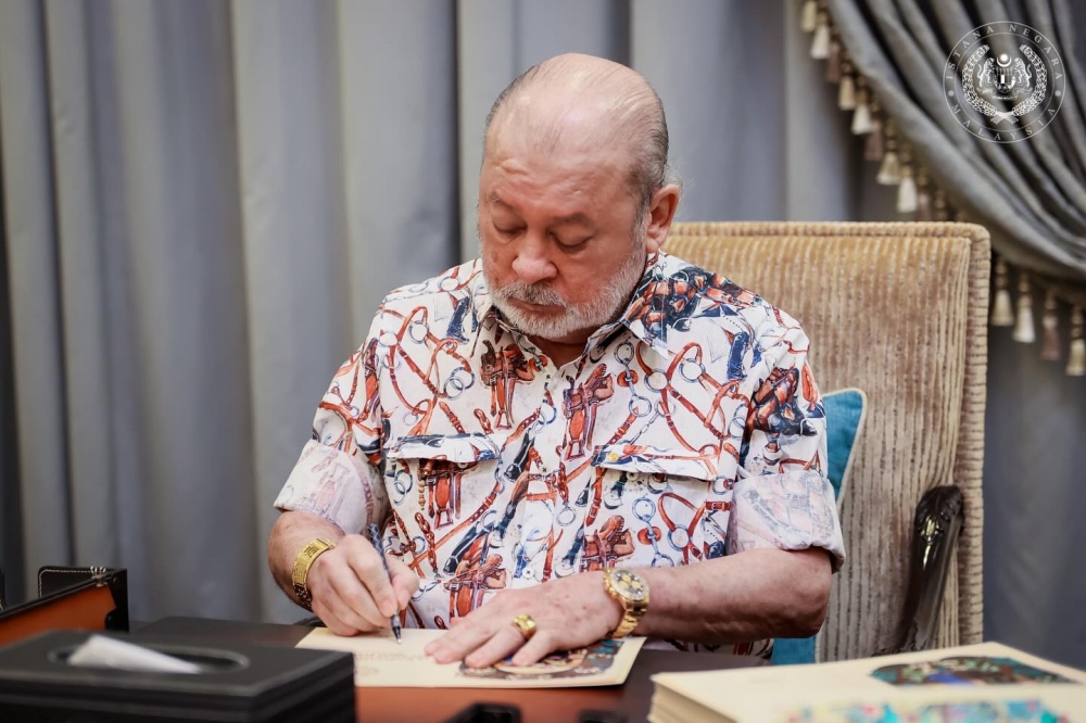 In a post on His Majesty’s official Facebook page, Sultan Ibrahim was seen signing Aidilfitri cards, which will be sent to selected recipients. — Picture via Facebook/Sultan Ibrahim Sultan Iskandar