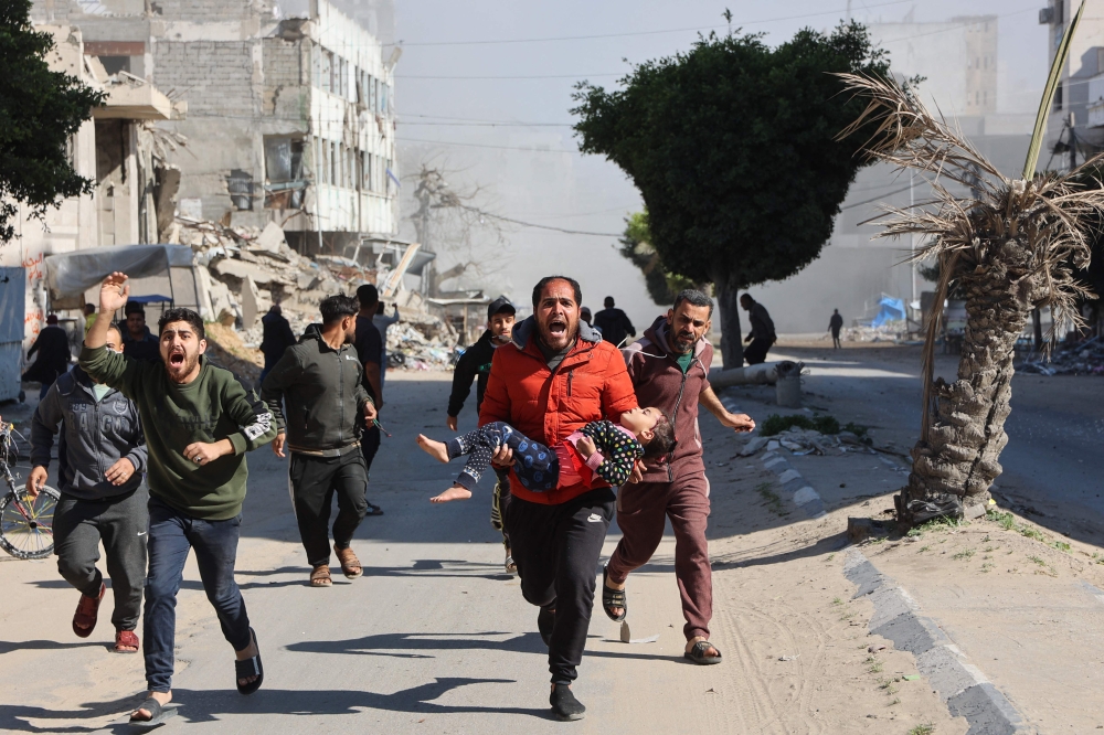 Palestinians rush an injured girl away from the site of Israeli strikes on a makeshift displacement camp in central Gaza City on March 23, 2025. — AFP pic
