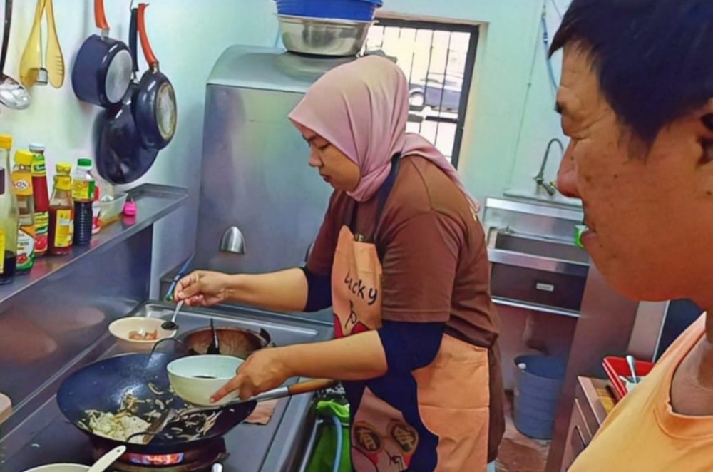 Lina learning how to make ‘char koay teow’ from the owner of Tiger Char Koay Teow. — Picture courtesy of Gimi Lim Burge