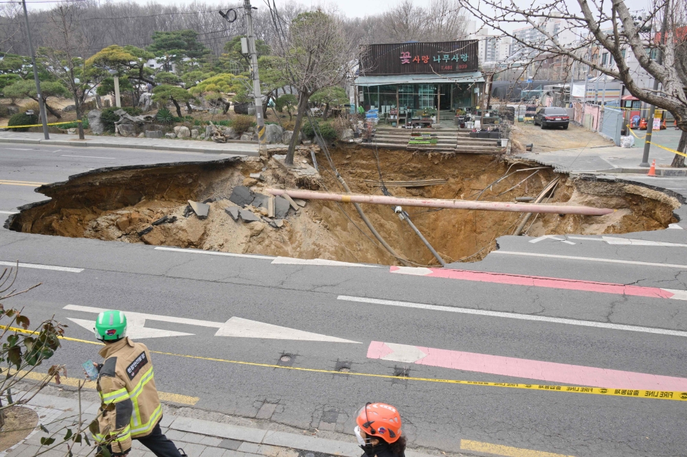 Rescue workers walk past a sinkhole outside a plant shop on a road in Seoul on March 25, 2025. — AFP pic 