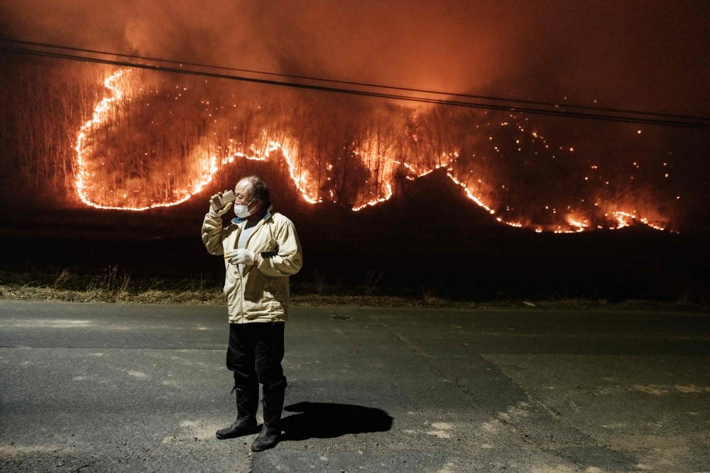 A man talks to his son on the phone under a streetlight on the road in front of his home as wildfires burn in Uiseong, South Korea, March 24, 2025. — AFP pic