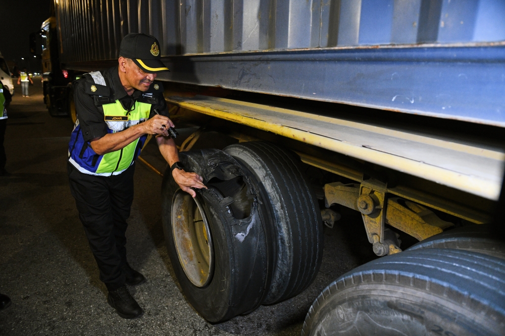 A Road Transport Department (JPJ) enforcement officer displays a retreaded container lorry tyre that had burst during a special operation held in conjunction with the 2025 Hari Raya Aidilfitri celebrations. — Bernama pic