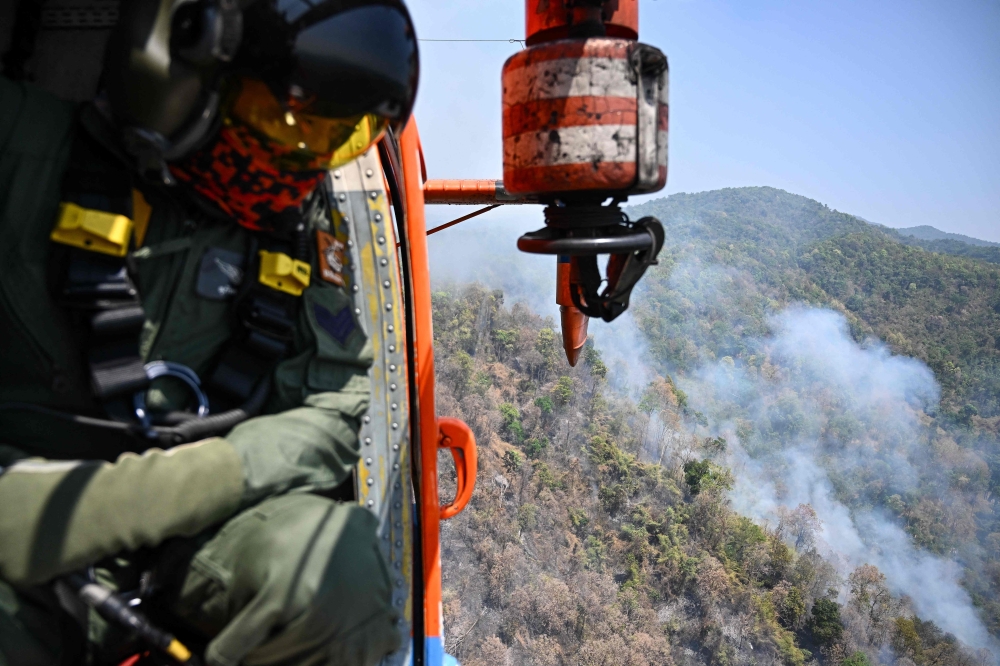 A Thai Department of Disaster Prevention and Mitigation (DDPM) personnel on a firefighting helicopter inspects fire spots to drop water to combat forest fires over Mae On district in the northern Thai province of Chiang Mai on March 26, 2025. Forest fires are burning in several areas of northern Thailand, contributing to the annual spike in air pollution that comes with farmers burning stubble to prepare their land for the next crop. — AFP pic