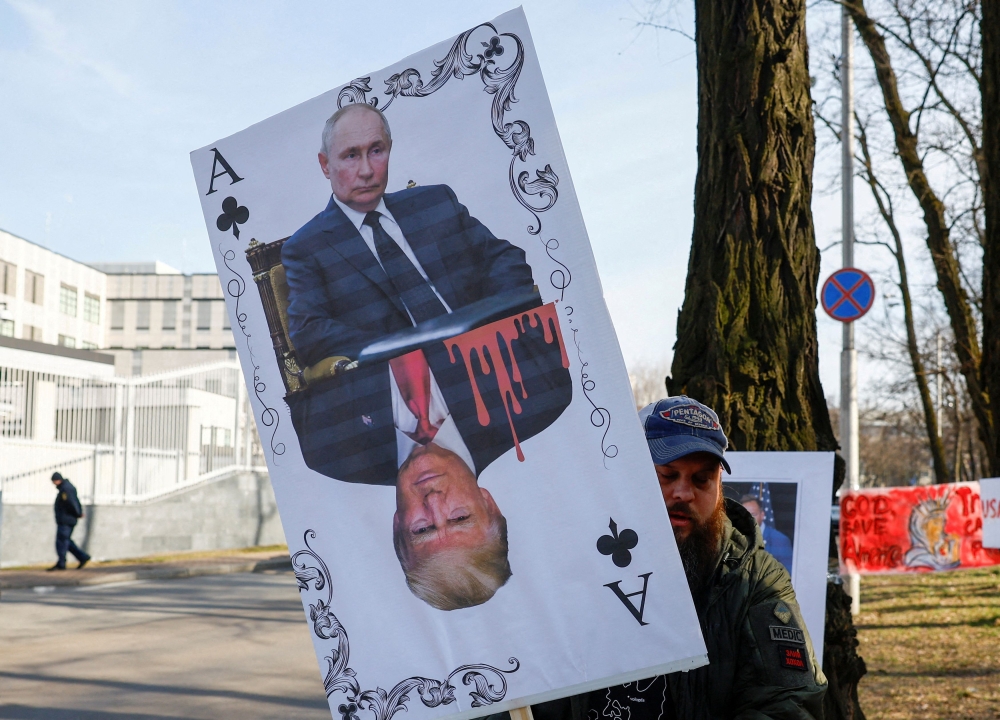 A demonstrator holds a banner depicting a playing card with portraits of Russian President Vladimir Putin and US President Donald Trump, in front of the US embassy in Kyiv, Ukraine March 8, 2025. — Reuters pic