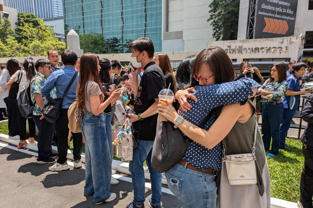 People stand outside an office building in Bangkok on March 28, 2025 after an earthquake. — AFP pic