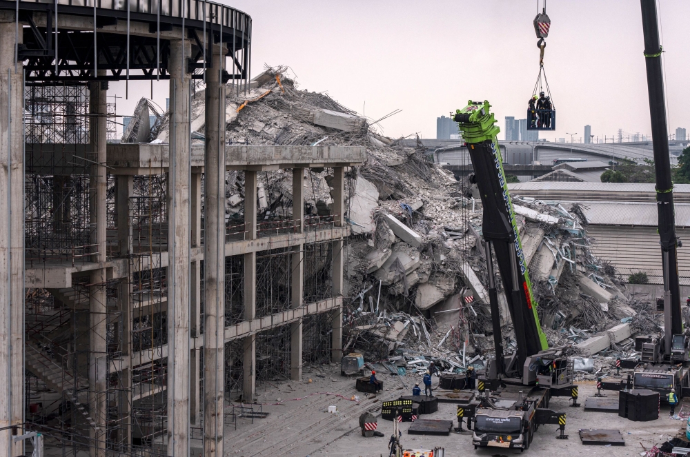 Rescue workers are lifted on a crane during search-and-rescue operations at the site of an under-construction building collapse in Bangkok. — AFP pic