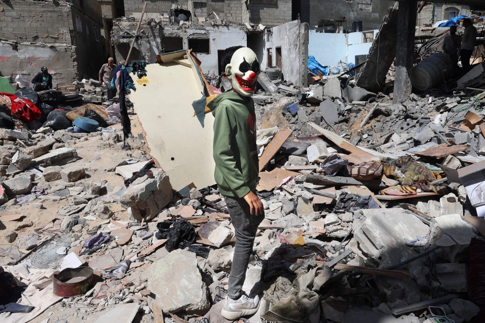 A Palestinian boy wearing a clown mask walks on the rubble of a house that was destroyed in an Israeli airstrike in Khan Younis. — AFP pic