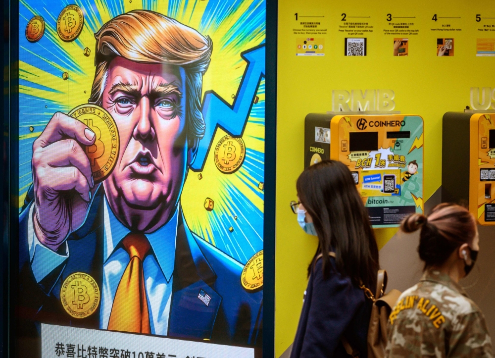 People walk past a cryptocurrency exchange office with a screen featuring US President Donald Trump holding cryptocurrency coins in Hong Kong on March 12, 2025. — File pic via AFP
