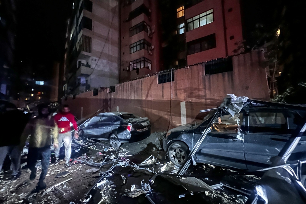 Residents walk past damaged cars after a building was hit by an Israeli strike in southern Beirut, early on April 1. — AFP pic