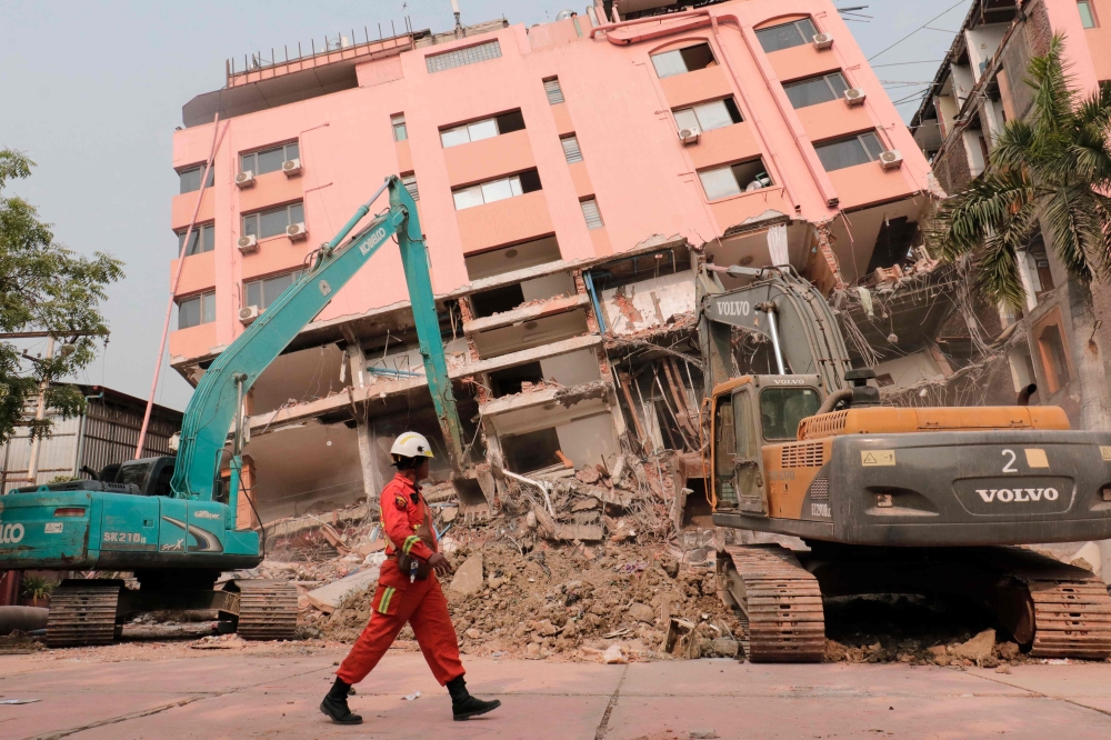 A rescue worker walks past heavy construction equipment being used to clear rubble at the site of a collapsed building in Mandalay on April 5, 2025, following the March 28 earthquake. — AFP pic