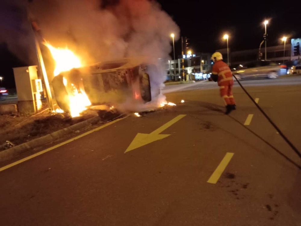 A firefighter works to extinguish the fire engulfing the car on the Samarahan Expressway. — Bomba pic via The Borneo Post 