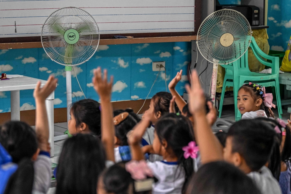 Students raise their hands in class in front of fans at an elementary school in Baseco, Manila on March 21, 2025. — AFP pic