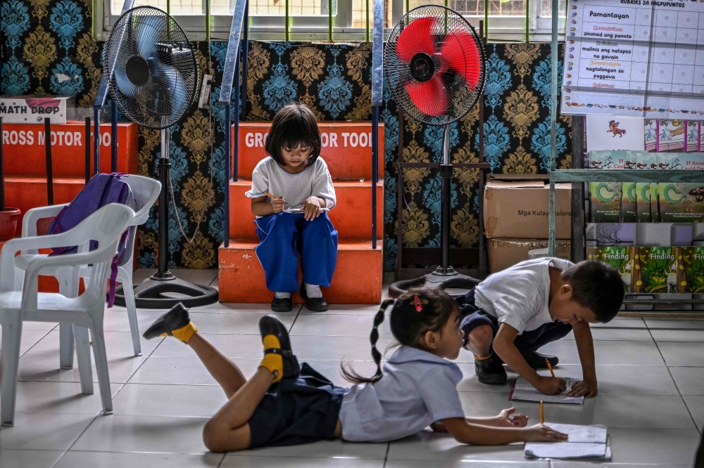 Students work on activities next to fans at an elementary school in Baseco, Manila on March 21, 2025. — AFP pic