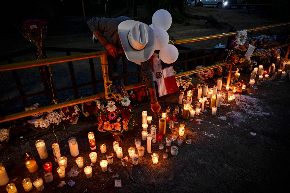 A man lights a candle as friends and relatives pay tribute to the victims in front of the Jet Set nightclub in Santo Domingo. — AFP pic