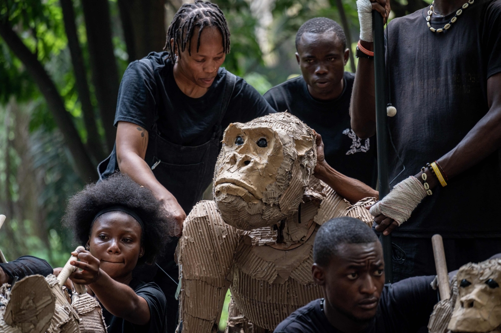 Puppeteer crouche next to a ife size animal puppet, part of the Herds public art and climate action project are  displayed in Kinshasa April 9, 2025.  — AFP pic