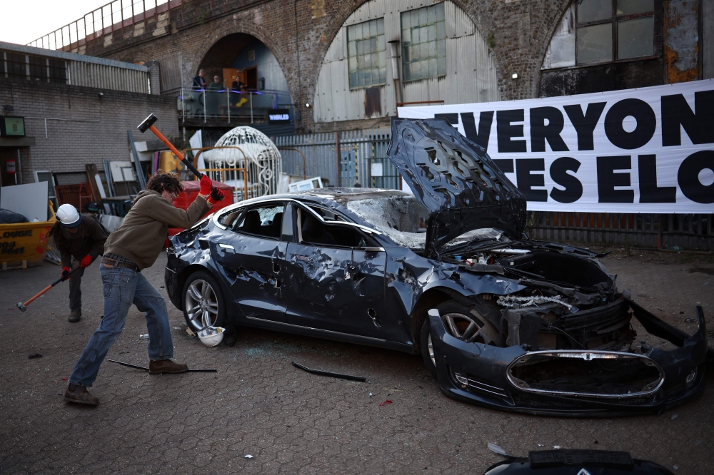 People smash a Tesla car during anti Elon Musk protest at Hardess Studios in south London on April 10, 2025.  — AFP pic