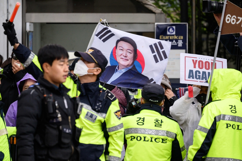 Police stand in front of pro-Yoon supporters on the side of a road as they wait for the arrival of former South Korean president Yoon Suk Yeol (pictured on flag) outside the Central District Court in Seoul on April 14, 2025. South Korean police raided Wednesday the Yoon’s office and his security detail, as part of a spiralling criminal probe into the impeached leader. — AFP pic 