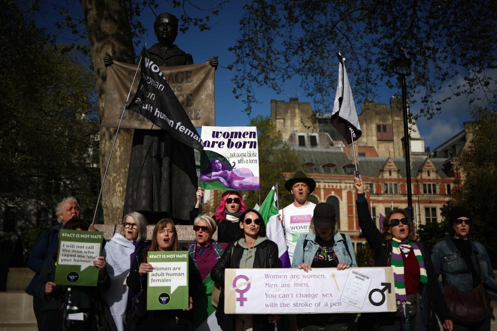 Activists sing as they hold placards including 'Women are born, not some bloke with a form' and 'Women are women, men are men, you can't change sex with the stroke of a pen' during a protest in Parliament Square. — AFP pic