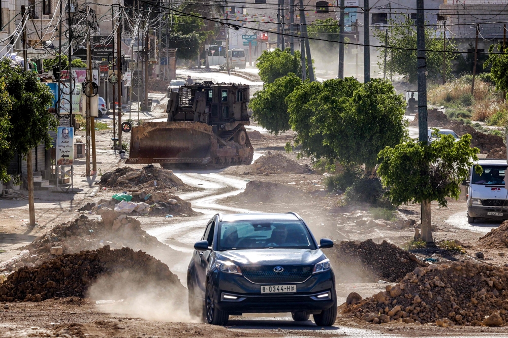 A vehicle moves along a partially-demolished road ahead of an Israeli military bulldozer during an army operation in the Palestinian refugee camps in Tulkarem in the northwest of the occupied West Bank on April 16, 2025. — AFP pic