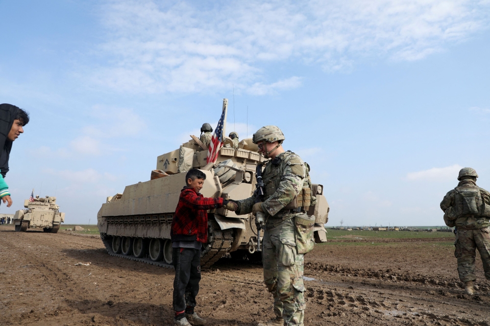 A soldier from the US-led coalition holds the hand of a boy during a joint U.S.- Kurdish-led Syrian Democratic Forces (SDF) patrol in the countryside of Qamishli in northeastern Syria February 8, 2024. — Reuters pic