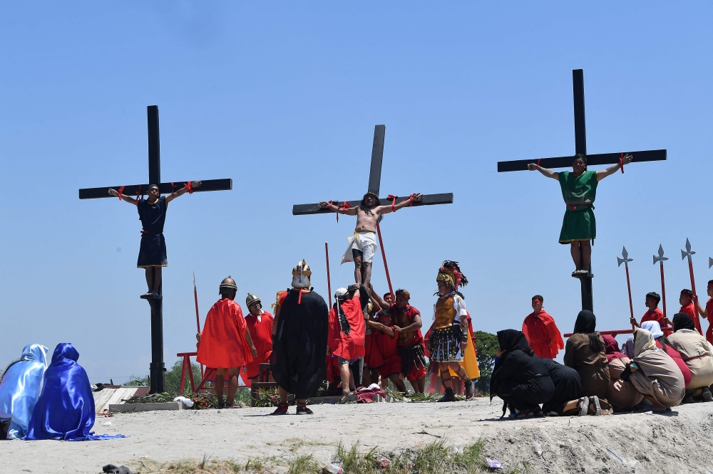 Penitent Ruben Enaje (centre) is raised after he was nailed to a cross during the observance of Lent in the village of Cutud in San Fernando City, Pampanga province April 18, 2025. — AFP pic