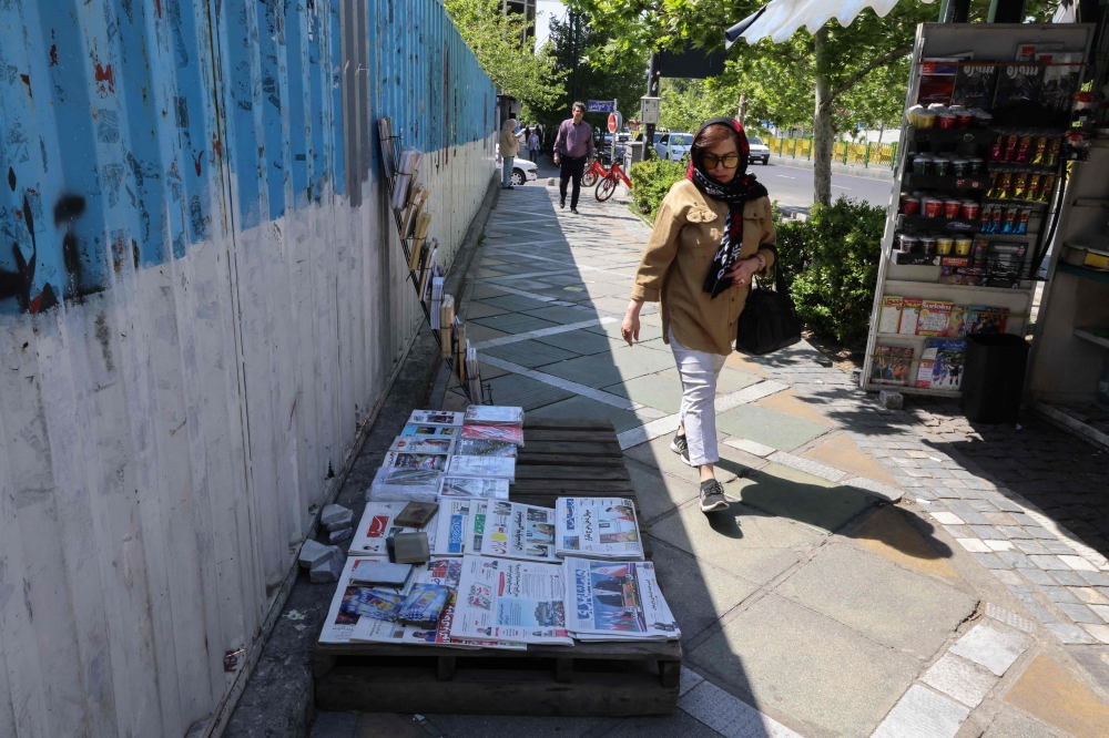 A woman walks past a newspaper stand at a kiosk in Tehran on April 19, 2025, featuring the Iran-US talks on the Iranian nuclear programme scheduled today. — AFP pic