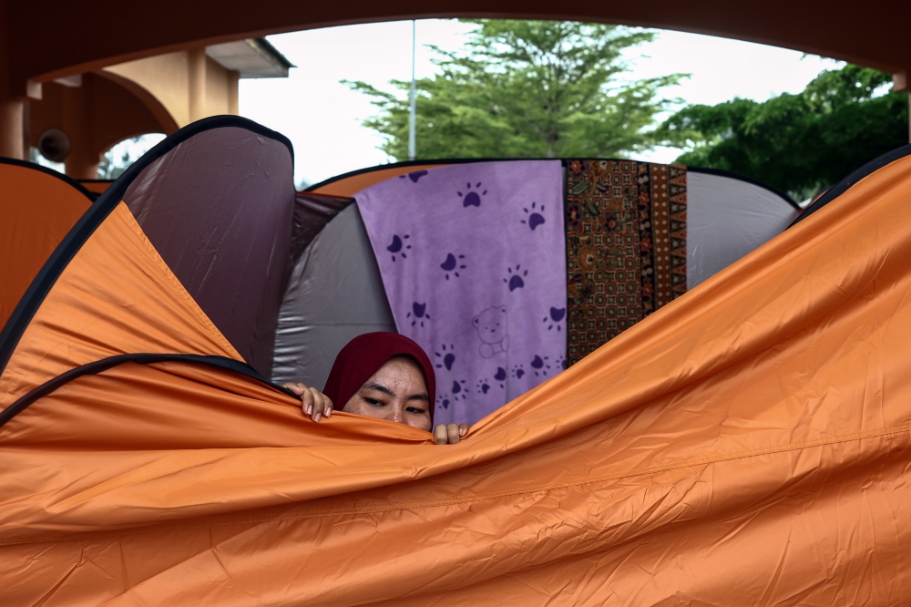 A person peeps over a tent at a temporary evacuation centre in the Mara Junior Science College in Tumpat, Kelantan, on Dec 7, 2024. — Bernama pic