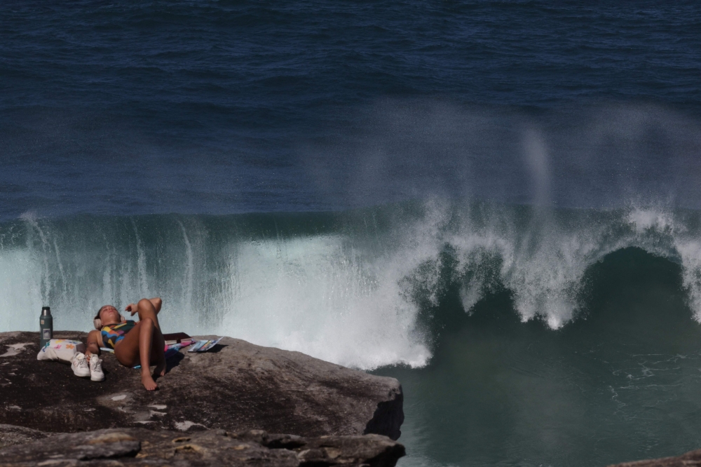 A tourist enjoys a sunny morning at Tamarama Beach as large waves crash against a rock in Sydney on April 18, 2025, amid powerful swells hitting Australia's east coast. — AFP pic
