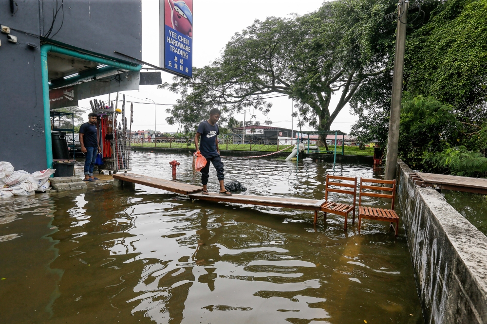 A man was seen crossing the make-shift bridge towards a shop as they wait for the flash flood to slowly reside after a thunderstorm here at Meru. — Picture by Sayuti Zainudin