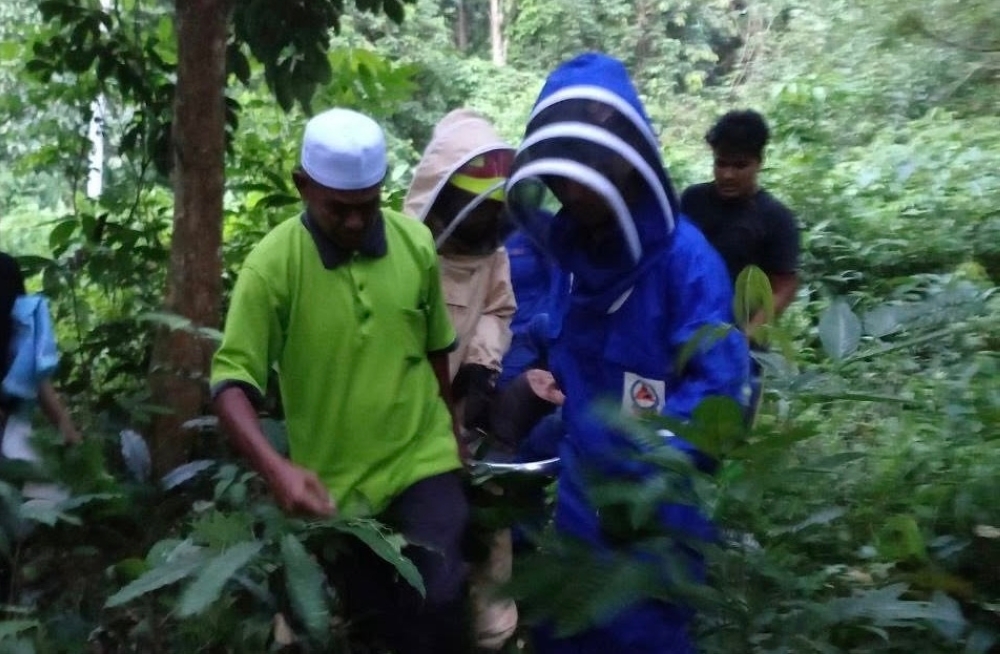 Civil Defence Force personnel, joined by local villagers, carefully carry one of the victims on a stretcher after the bee attack near a forest by Kampung Bandar Charuk Sotong, Baling. — Picture via Facebook