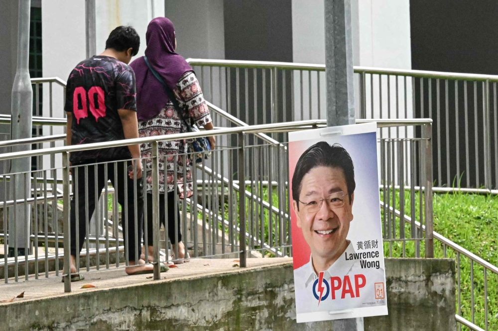 Pedestrians walk past a poster of Singapore's Prime Minister and secretary-general of the ruling People's Action Party (PAP) Lawrence Wong displayed on a lamp post ahead of the general election in Singapore on April 23, 2025. — AFP pic