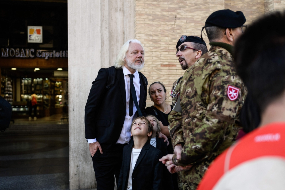 WikiLeaks founder Julian Assange (left) speaks with a member of the military forces in Via della Conciliazione by St Peter's Square in The Vatican on April 26, 2025 during late Pope Francis' funeral ceremony. — AFP pic