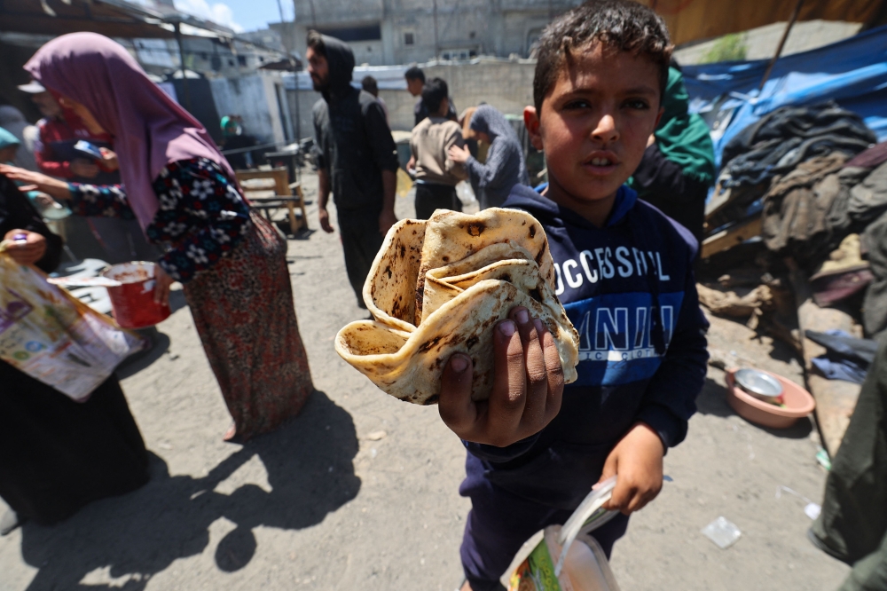 A Palestinian boy carries a portion of freshly-baked bread received from a charity kitchen run by the United Nation’s World Food Programme (WFP) at the Nuseirat refugee camp in the central Gaza Strip April 26, 2025. — AFP pic