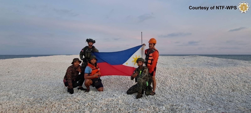 This handout photo taken on April 27, 2025, received on April 28 and released by the National Task Force on West Philippine Sea (NTF-WPS) through Philippine Coast Guard shows Philippine coast guard and military personnel holding a Philippine flag during an inter-agency maritime operation in Sanday Cay 2. — National Task Force on West Philippine Sea (NTF-WPS) handout pic via AFP 