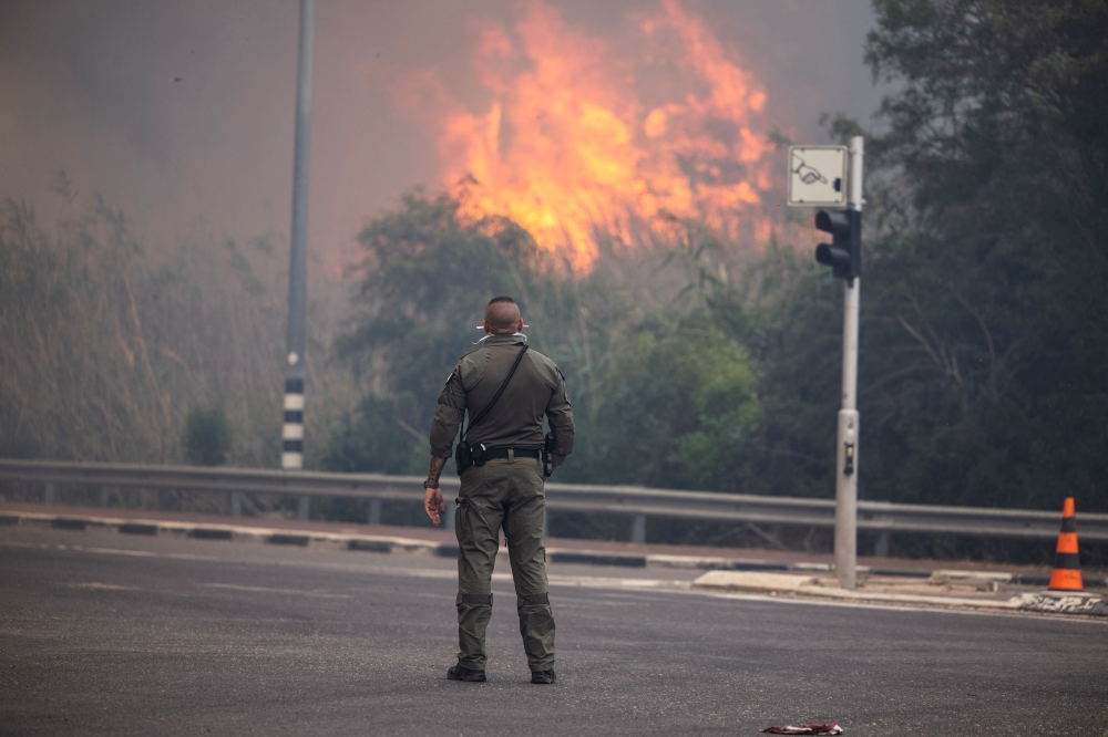 A security member stands while smoke and flame rise, as wildfires caused by extreme heat and winds broke out in central Israel, near Latrun, Israel, April 30, 2025. — Reuters pic 